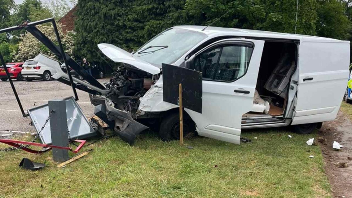 White van with destroyed frontage lodged into pub sign on grass