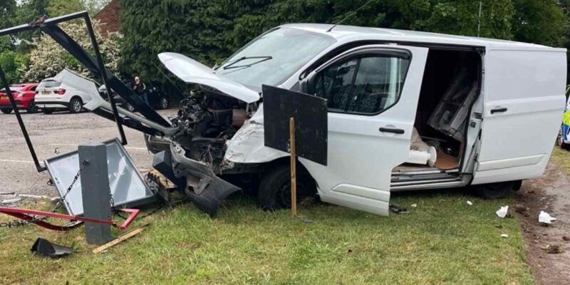 White van with destroyed frontage lodged into pub sign on grass